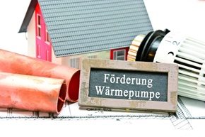 Modellhaus mit Heizkörperthermostat und einem Schild mit der Aufschrift Förderung Wärmepumpe